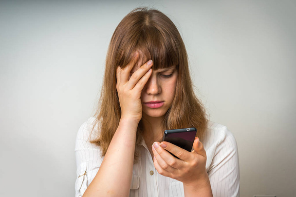 Разочарованная женщина держит и смотрит на мобильный телефон
 - Фото, изображение