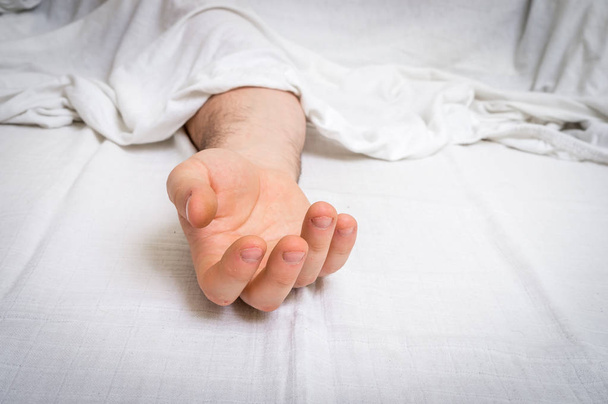 De dead man's lichaam onder witte doek met focus op hand - Foto, afbeelding