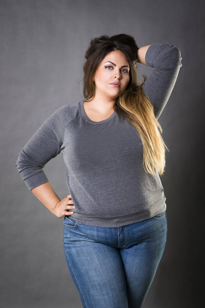 Young beautiful plus size model in blue jeans, xxl woman on gray background - Photo, image
