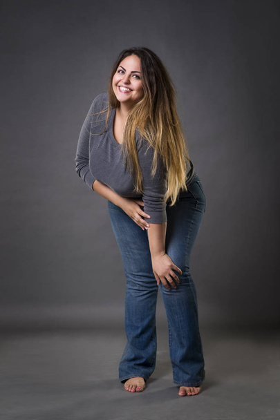 Young beautiful plus size model in blue jeans, xxl woman on gray studio background - Фото, изображение