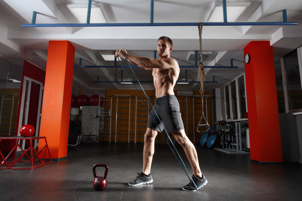 Fitness man exercising with stretching elastic rubber band in the gym - Foto, Imagen