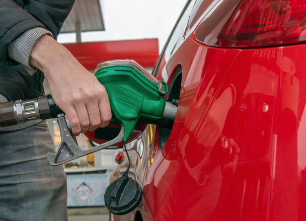 Mies pumppaa bensaa punaisella autolla huoltoasemalla.
. - Valokuva, kuva