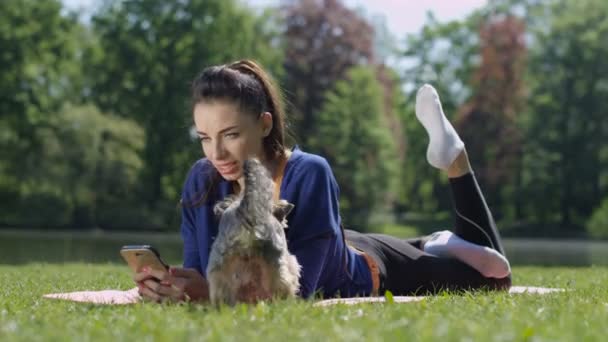 Young attractive woman lying on mat and using phone in sunny park.  - Metraje, vídeo