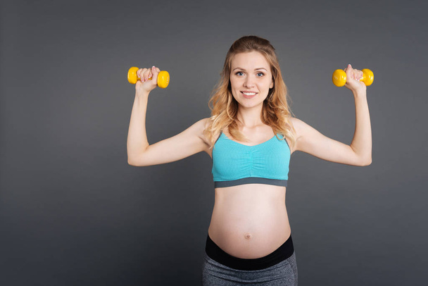 Attractive pregnant female using a dumbbell while training - Foto, Bild
