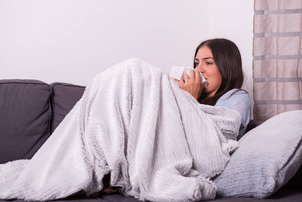Молодая женщина лежит больной на диване дома
 - Фото, изображение