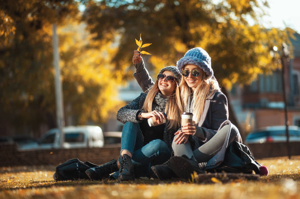 Kahve içme ve gülüyor çimenlerin üzerinde parkta oturan iki güzel mutlu kadın. Kavram dostluk, beraberlik, mutluluk. - Fotoğraf, Görsel