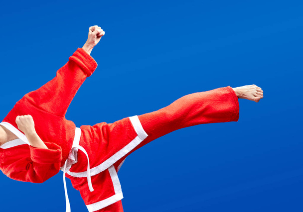 Con cinturón blanco y en un traje de Santa Claus la deportista está golpeando patadas
 - Foto, imagen