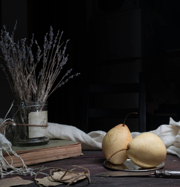 still life. pear, old books and a bunch of lavender on a dark background - Photo, image