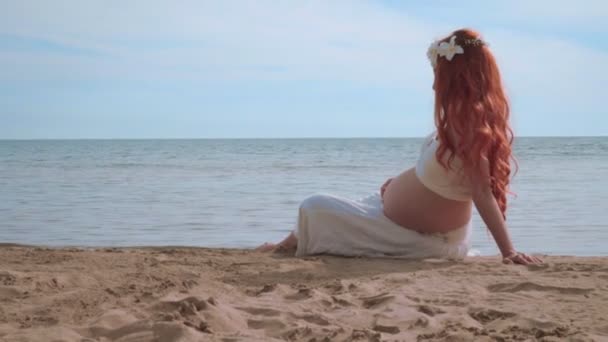 Беременная женщина на пляже, вид сбоку. Женщина, сидящая на морском хребте
. - Кадры, видео