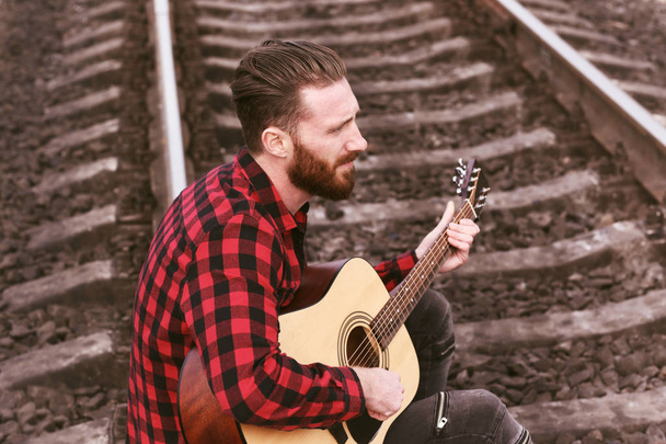 Handsome man playing guitar on railroad - Photo, Image