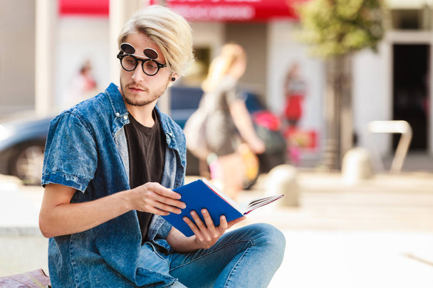 Hipster guy holding notebook sitting on ledge - Foto, afbeelding