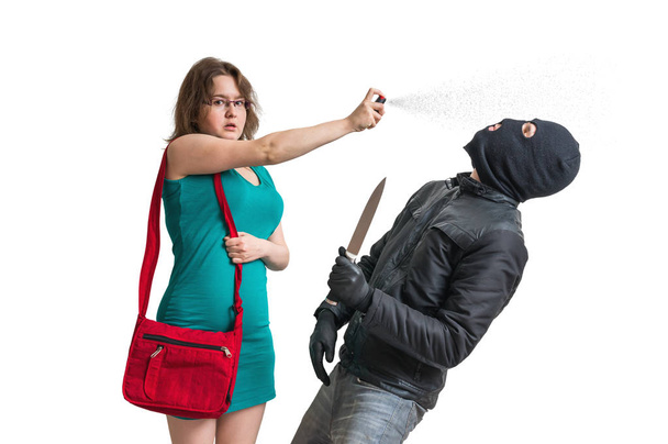 Jonge vrouw verdedigt met pepperspray tegen gewapende dief met mes. Geïsoleerd op witte achtergrond. - Foto, afbeelding