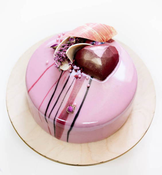 Minimalistic pink mousse cake with coated with mirror glaze on a white background. Chocolate heart, chocolate swirl and dry heather decor. - Photo, Image