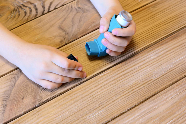 Un niño pequeño abre el inhalador de asma. Tratamiento por inhalación de enfermedades respiratorias. Medicamentos para la alergia y el asma bronquial. Antiguo fondo de madera
  - Foto, imagen