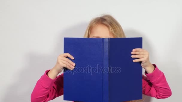 Dívka vypadá z knihy. Malá dívka špioni z velké knihy. Blondy dívka drží otevřená velká modrá kniha. - Záběry, video