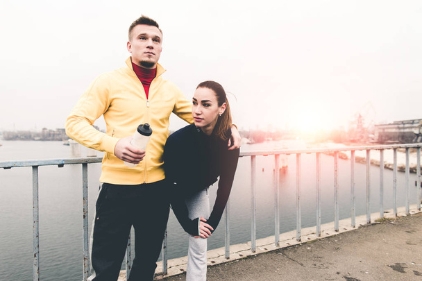 Couple young athletes in sports clothing standingg on city bridg - Photo, Image