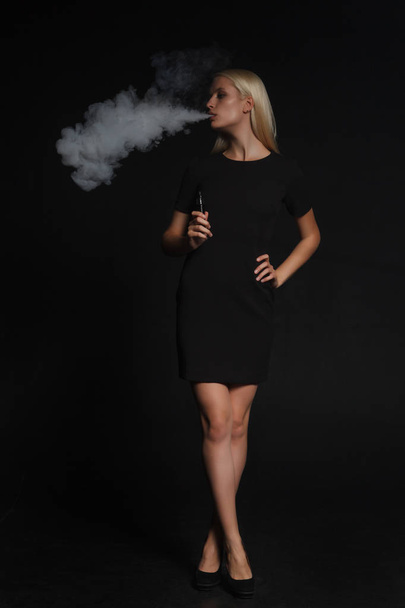 Frau im schwarzen Kleid raucht eine elektronische Zigarette - Foto, Bild