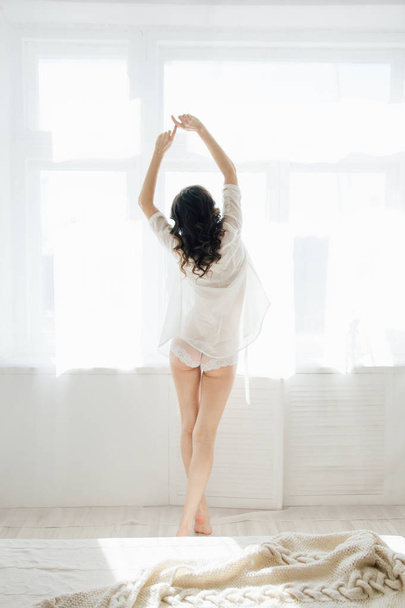 Mulher acorda e puxa de pé na janela pela manhã
 - Foto, Imagem