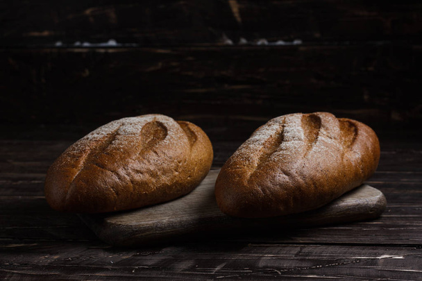 Two black bread with flour on a wooden background. Advertising bread. Leaning flour. - Photo, Image