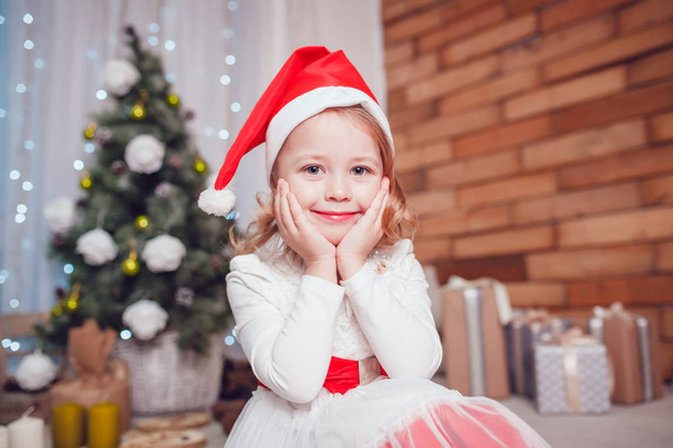 Smiling little girl in Santas hat sitting in Christmas decoration. New Year. - Valokuva, kuva