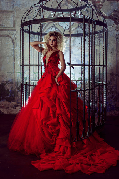 Moda rubia en vestido rojo con falda esponjosa cerca de la jaula de los pájaros, concepto de liberación
 - Foto, imagen