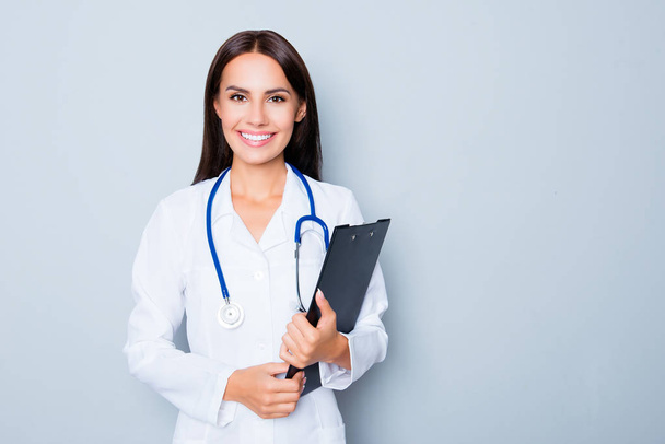 Cheerful female doctor in white uniform holding clipboard - Foto, Bild