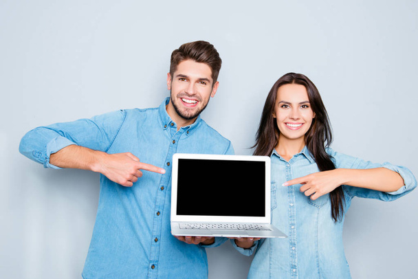 Happy man and woman showing laptop and pointing on black screen - 写真・画像