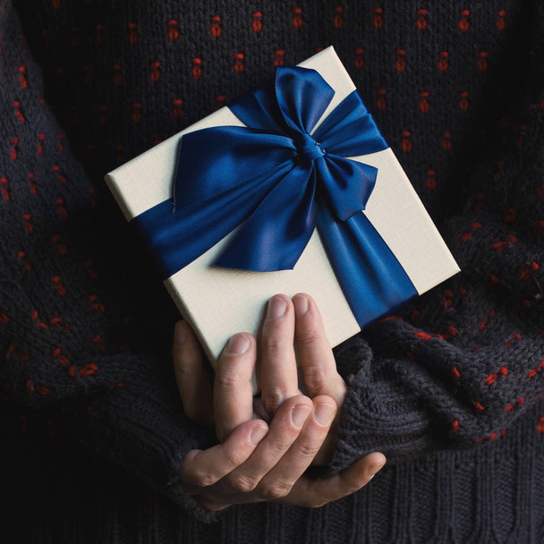 Close up van een man in de trui bedrijf van een gift met blauw lint beh - Foto, afbeelding