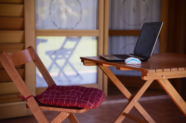Nomad werk concept afbeelding met computer op houten tafel en zonlicht, wazig bomen van natuur park achtergrond en zomer seizoen - Foto, afbeelding