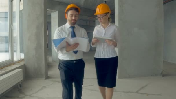 Business people, man and woman discussing construction plan, walking at a construction site. Steadycam shot. - Video