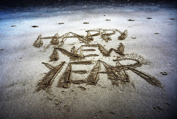 Frohes neues Jahr auf Sand geschrieben bei Sonnenuntergang.  - Foto, Bild