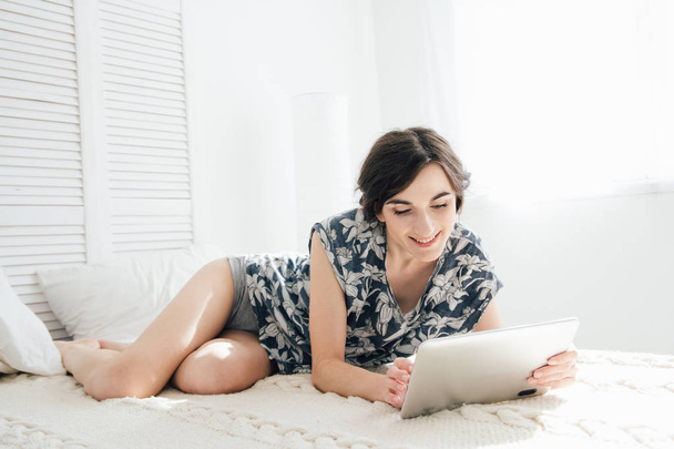 Девушка смотрит на планшет в постели
  - Фото, изображение