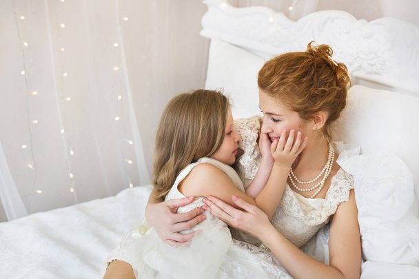 Portrait of mother with little daughter on a bed - Fotoğraf, Görsel