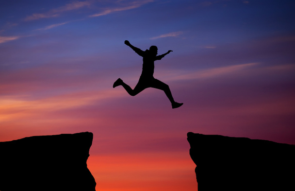 Man jumping across the gap from one rock to cling to the other.  - Photo, Image