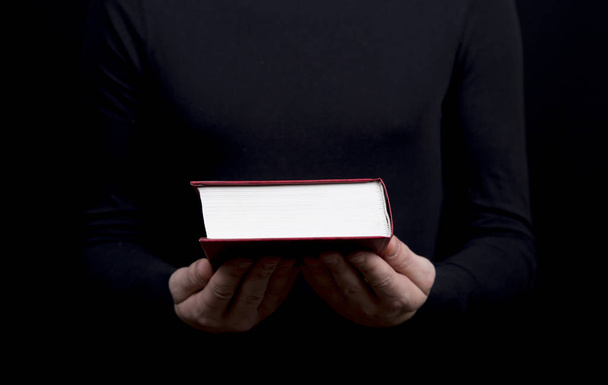 mężczyzna ubrany w czarny trzyma książkę w czerwoną obwolutą  - Zdjęcie, obraz