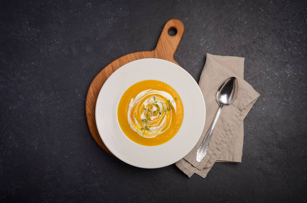 Pumpkin cream soup with cream and thyme on black background - Foto, imagen