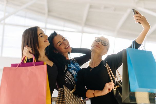 Attractive pretty women taking selfie after shopping. Girls are very happy, smiling. They posing for photos. Have many shopping bags - Foto, Bild