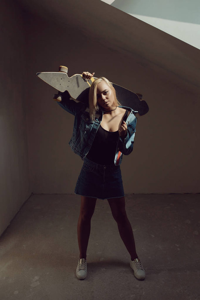 Pretty blonde woman with longboard in dark room - Fotó, kép