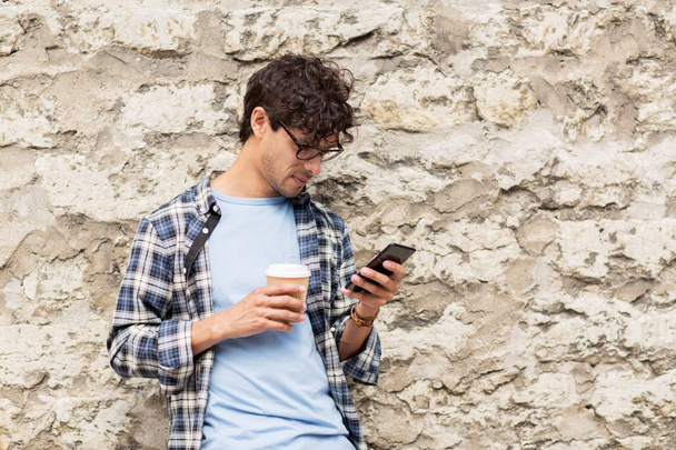 man with smartphone drinking coffee on city street - Фото, зображення