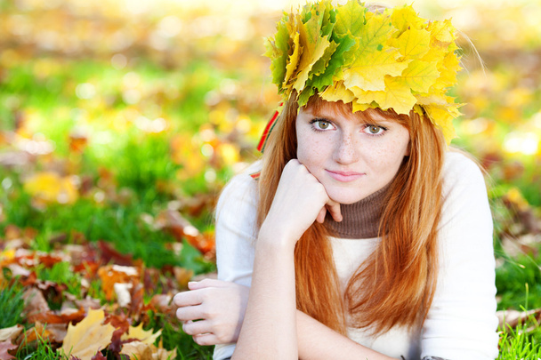 young redhead teenager woman in a wreath of maple leaves lying o - Φωτογραφία, εικόνα