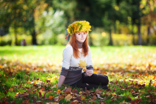 Молодая рыжая девушка-подросток в венке из кленовых листьев сидит
 - Фото, изображение