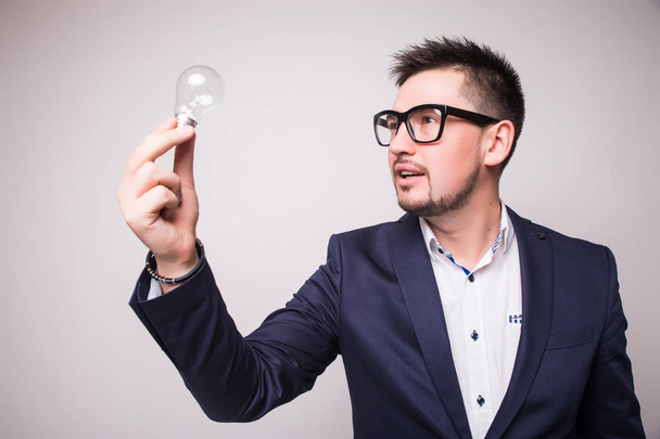 Serious bearded young businessman standing and looking at light bulb - Foto, afbeelding