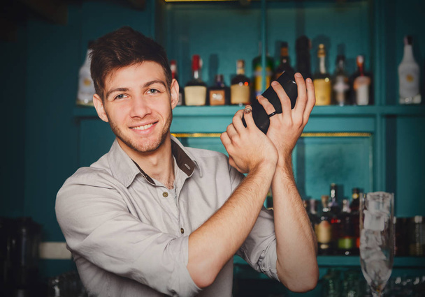 Jonge knappe barman in bar schudden en mengen van alcohol cocktail - Foto, afbeelding