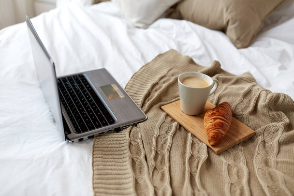 laptop, coffee and croissant on bed at cozy home - Zdjęcie, obraz