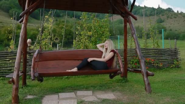 Młoda kobieta odpocząć na dużym drewnianym tarasem huśtawka - Materiał filmowy, wideo