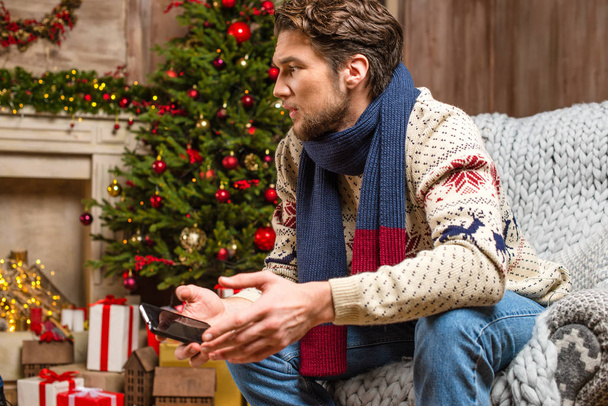 Man in knitted sweater holding smartphone - Фото, изображение