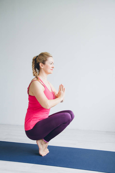 Mujer joven en una habitación blanca haciendo ejercicios de yoga
 . - Foto, imagen