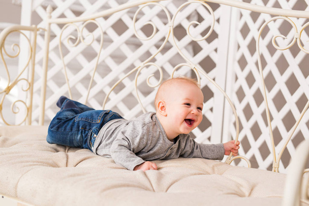 Rozkošný smějící se chlapeček v bílé a prosluněná ložnice. Novorozené dítě, relaxační. Rodinné ráno doma. - Fotografie, Obrázek