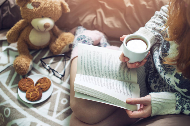 Девушка читает книгу в постели с теплыми носками пьет кофе
 - Фото, изображение