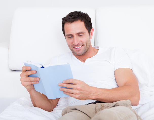 Portrait Of Young Man Reading Book On Bed - Foto, imagen